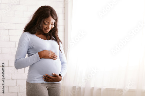 Canvas Print Peaceful pregnant afro woman hugging her tummy at home