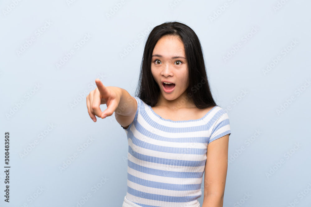 Teenager asian girl over isolated blue background pointing away Teenager asian girl over isolated blue background pointing away