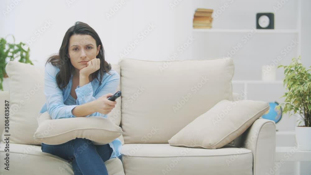 Slowmo. Attractive woman is bored by watching TV, sitting on sofa at home. Suddenly she hears surprising information. Copy space. 4K. Slowmo. Attractive woman is bored by watching TV, sitting on sofa at home. Suddenly she hears surprising information. Copy space. 4K.