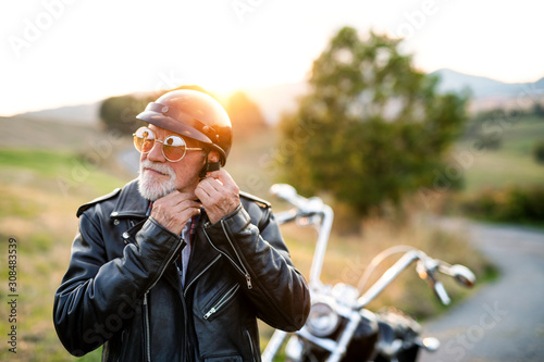 Foto A senior man traveller with motorbike in countryside, putting on helmet