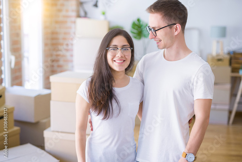 Young beautiful couple wearing glasses standing at new home around cardboard boxes
