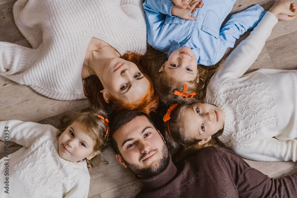 Top view cute little girls and their beautiful young parents look at the camera and smile while lying on the floor of the house. the concept of family happiness. large family - obrazy, fototapety, plakaty 