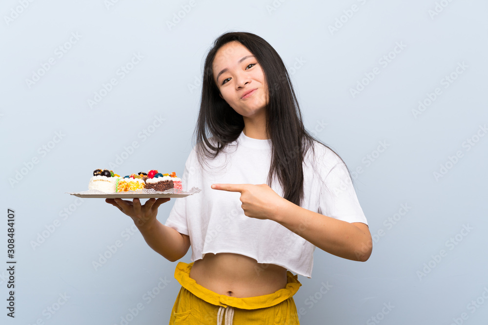 Teenager asian girl holding lots of different mini cakes and pointing it Teenager asian girl holding lots of different mini cakes and pointing it