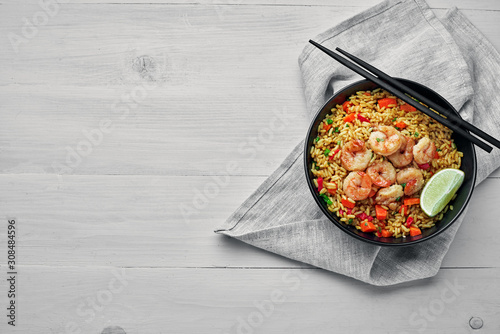Shrimp fried rice with vegetables, green onions and lime in a black pottery bowl. Traditional Thai meal on a white table with fabric tablecloth. Top view, directly above shot with space for text.