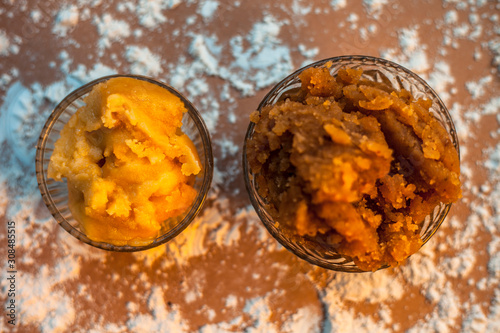 Close up of Indian Gujarati popular dish Atte ka sheera or Halwa-Karah parshad in a glass bowl on a brown surface with some spread wheat flour and some jaggery in a glass bowl. Horizontal top shot. photo