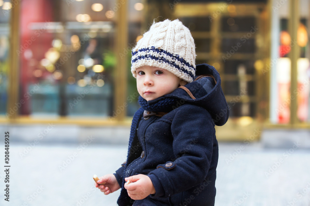 Fashion toddler boy with teddy bear toy, eating traditional Czech sweet pastry, called trdlo in the city center Fashion toddler boy with teddy bear toy, eating traditional Czech sweet pastry, called trdlo in the city center