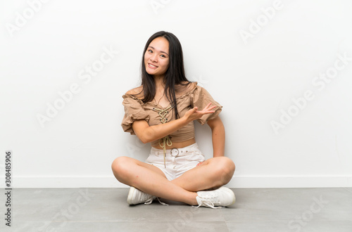 Teenager asian girl sitting on the floor extending hands to the side for inviting to come