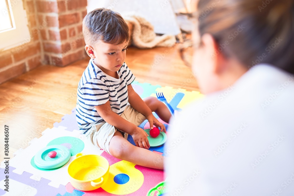 Beautiful toddler boy sitting on puzzle playing with plastic plates, fruits and vegetables at kindergarten Beautiful toddler boy sitting on puzzle playing with plastic plates, fruits and vegetables at kindergarten