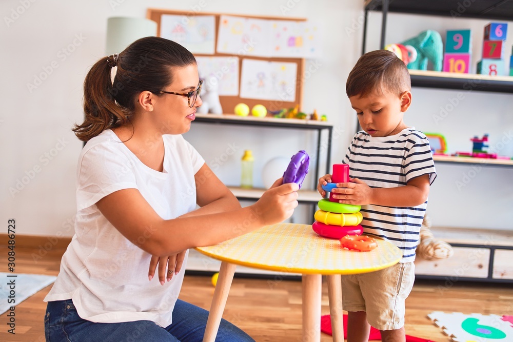 Beautiful teacher and toddler boy building pyramid with hoops bolcks at kindergarten Beautiful teacher and toddler boy building pyramid with hoops bolcks at kindergarten