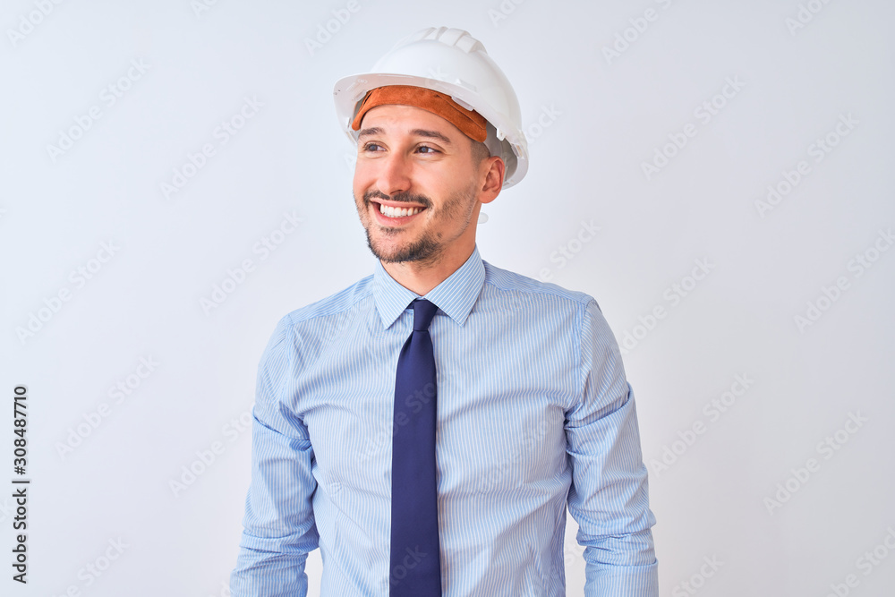 Young business man wearing contractor safety helmet over isolated background looking away to side with smile on face, natural expression. Laughing confident. Young business man wearing contractor safety helmet over isolated background looking away to side with smile on face, natural expression. Laughing confident.