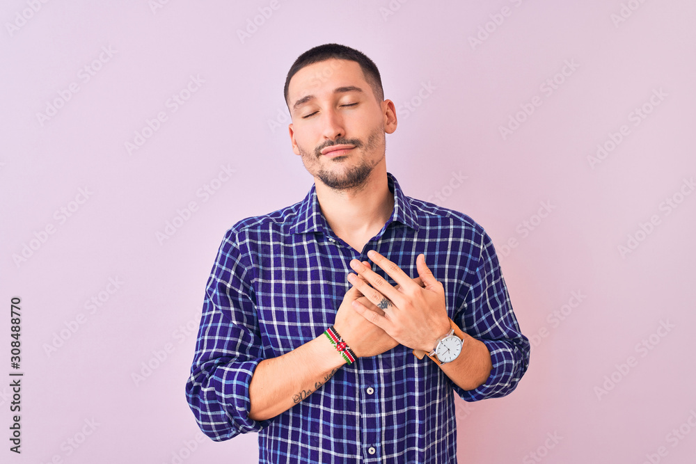 Young handsome man standing over isolated background smiling with hands on chest with closed eyes and grateful gesture on face. Health concept. Young handsome man standing over isolated background smiling with hands on chest with closed eyes and grateful gesture on face. Health concept.