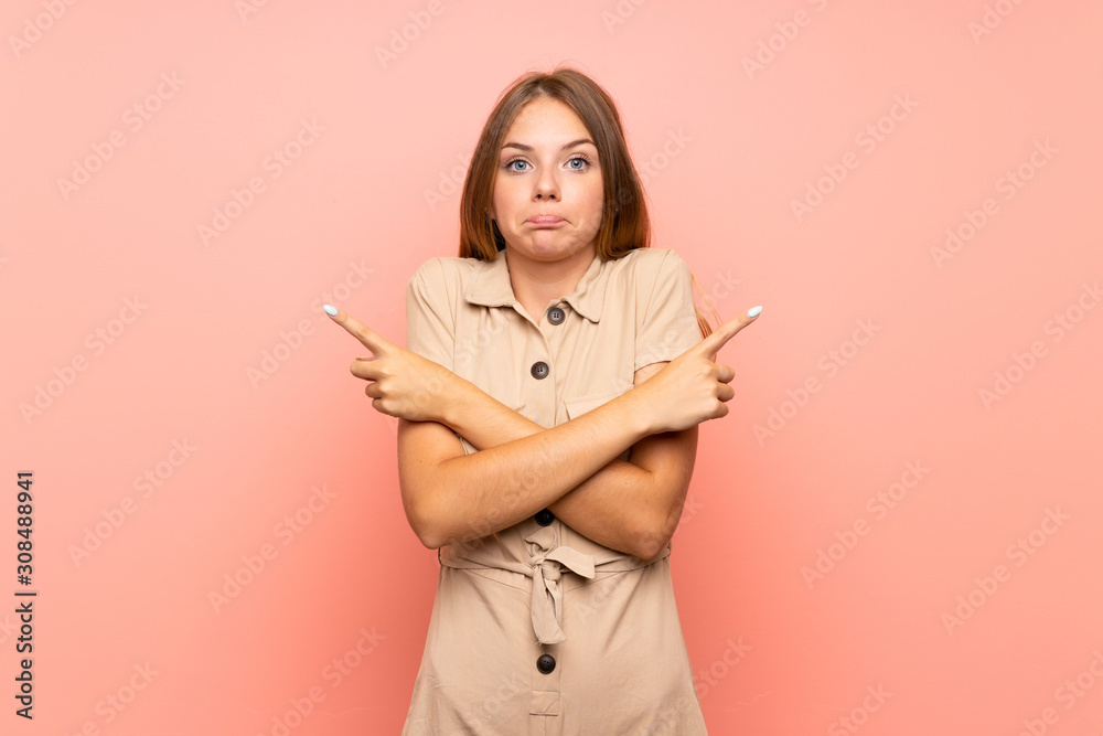 Lithuanian blonde girl over isolated pink background pointing to the laterals having doubts Lithuanian blonde girl over isolated pink background pointing to the laterals having doubts