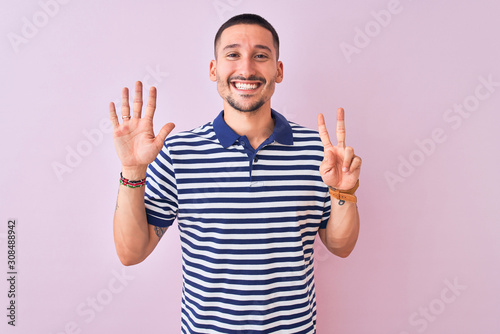 Young handsome man wearing nautical striped t-shirt over pink isolated background showing and pointing up with fingers number seven while smiling confident and happy.