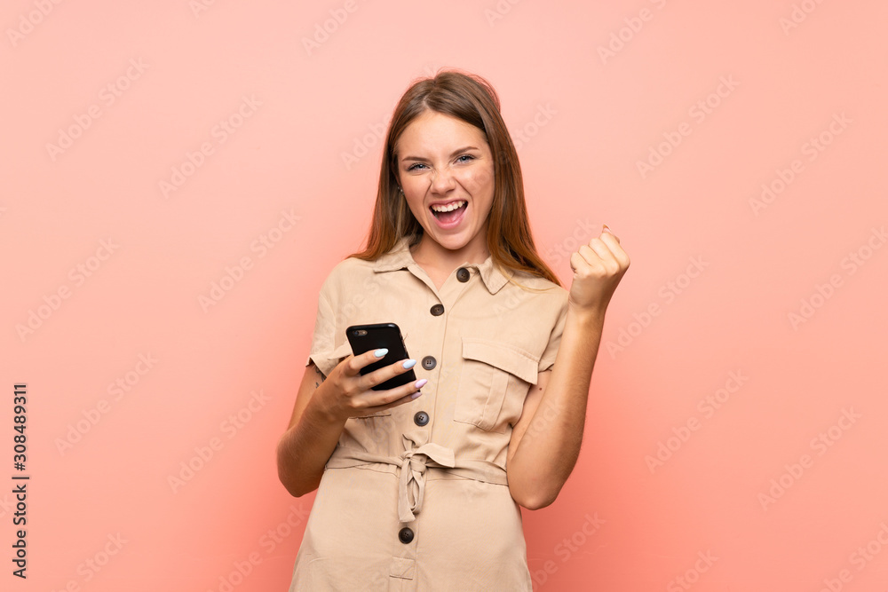 Lithuanian blonde girl over isolated pink background with phone in victory position Lithuanian blonde girl over isolated pink background with phone in victory position
