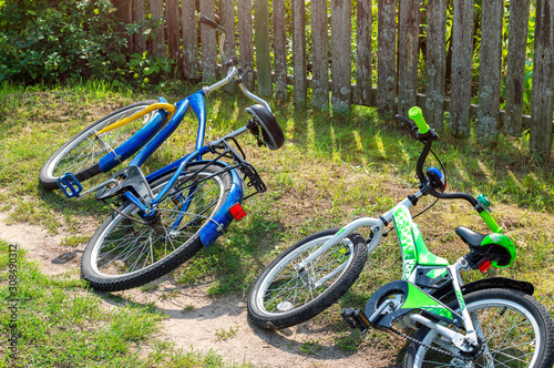 Children's and adult bicycles lay in the grass on the side of the road near a rural fence. Country trips on the weekend