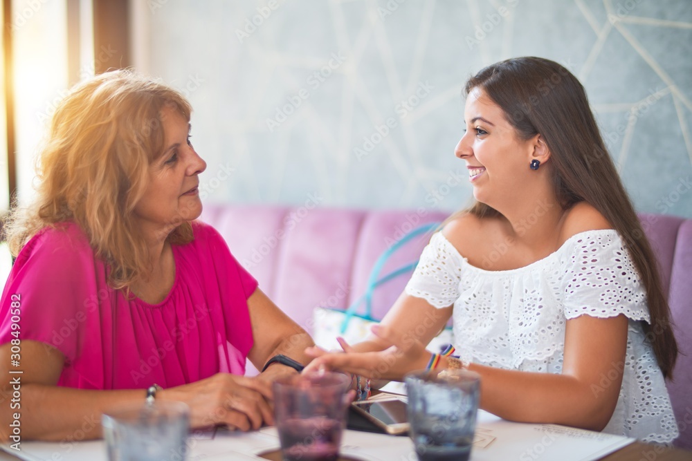 Beautiful mother and daugther sitting at restaurant speaking and smiling Beautiful mother and daugther sitting at restaurant speaking and smiling
