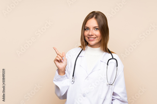 Young blonde woman over isolated background with doctor gown and pointing side