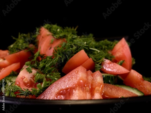 Vegetable salad of cucumbers, tomatoes and herbs on a black background. Finely chopped vegetables in a salad bowl, close-up. Concept: healthy diet, fresh vegetables, vitamins.