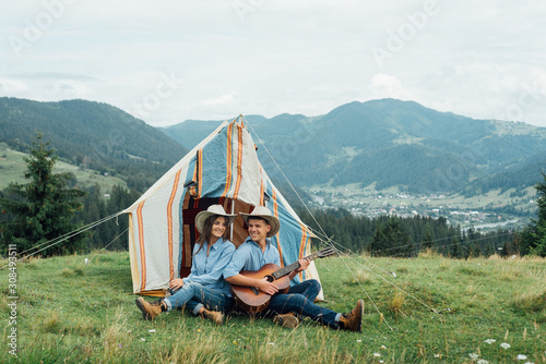 Camping couple in tent sitting looking at view in mountains . Campers smiling happy outdoors in mountains. Couple having fun relaxing after outdoor activity.