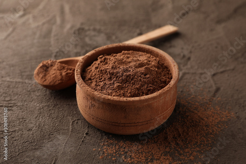 Bowl with cocoa powder and spoon on brown background, closeup