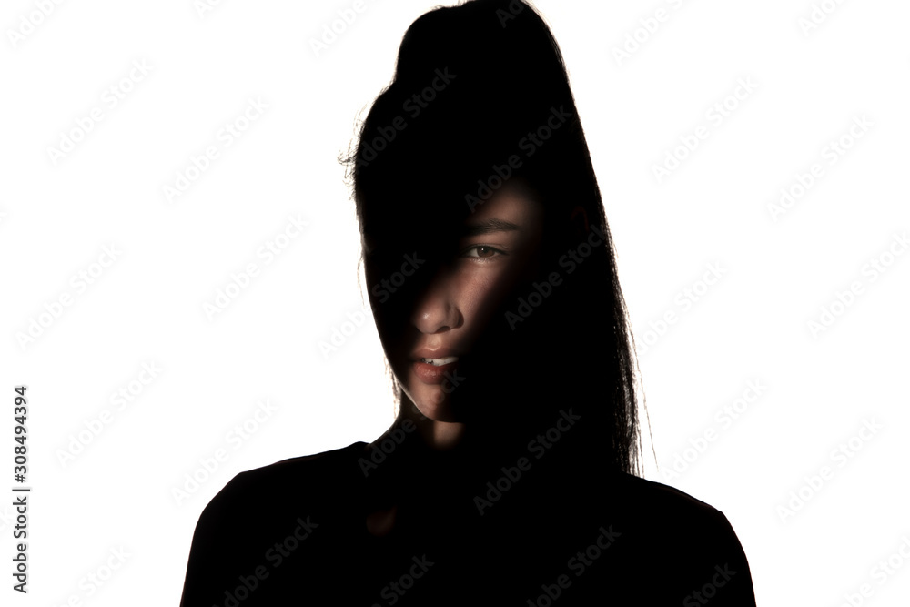 Dramatic portrait of caucasian young girl in the dark isolated on white studio background. Sunlight line on the dark face. Human nature, hidden things, psycology concept. Art elegant creative photo.