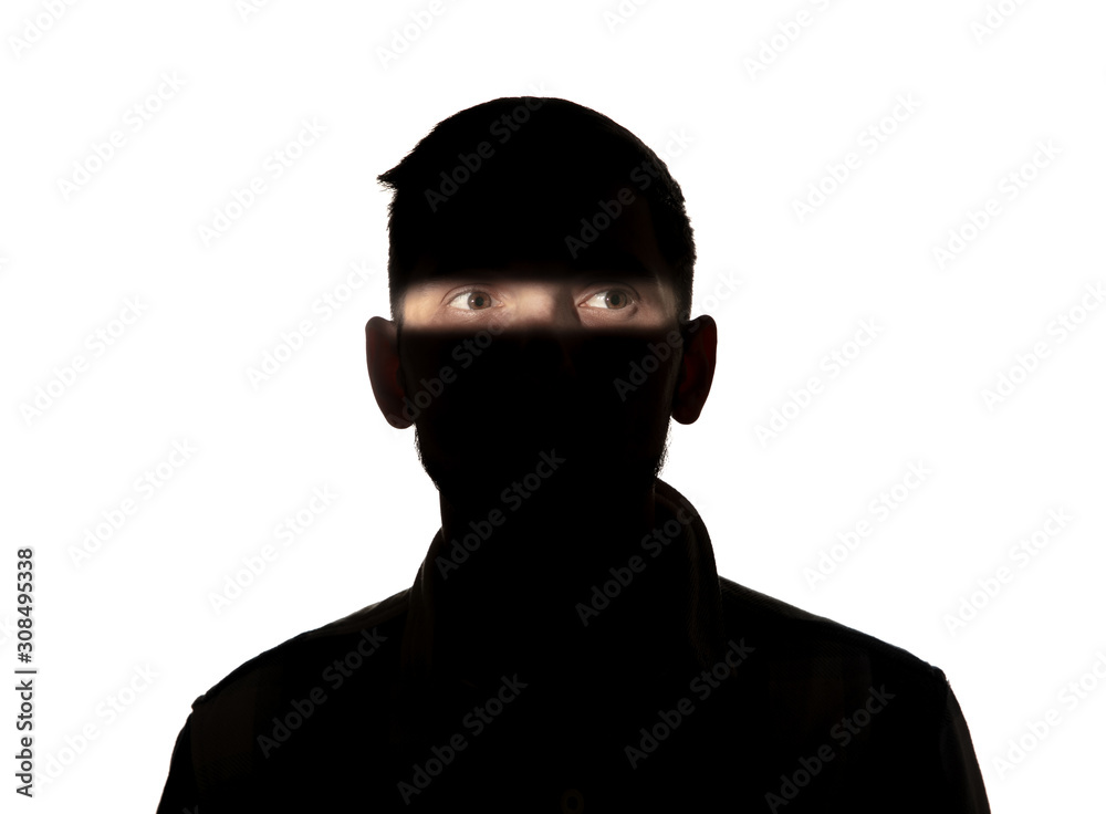 Dramatic portrait of caucasian young man in the dark isolated on white studio background. Sunlight line on the dark face. Human nature, hidden things, psycology concept. Art elegant creative photo. Dramatic portrait of caucasian young man in the dark isolated on white studio background. Sunlight line on the dark face. Human nature, hidden things, psycology concept. Art elegant creative photo.