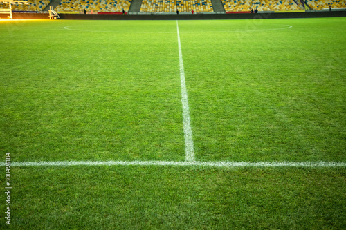 Football field with green grass and marking. Soccer field. White line markings on the field. Places for the audience in the distance.
