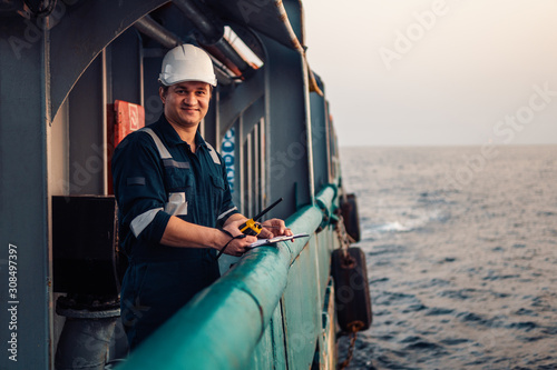 Deck Officer on deck of offshore vessel or ship , wearing PPE personal protective equipment. He fills checklist. Paperwork at sea photo