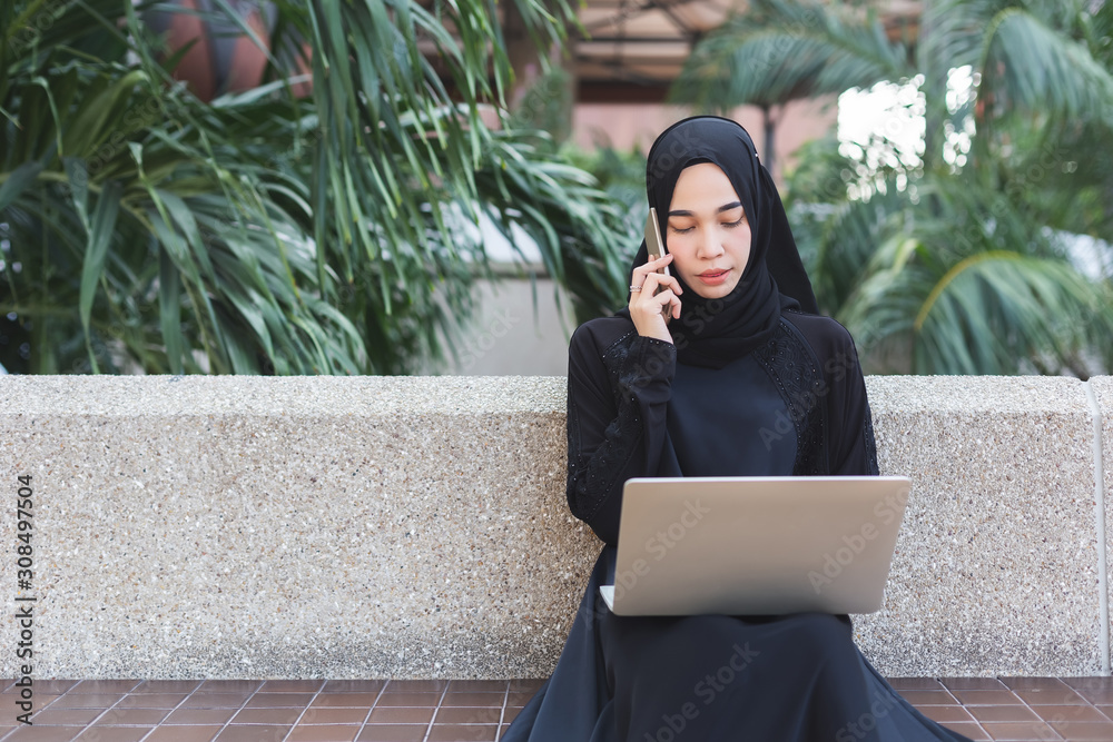 muslim woman in black hijab talking telephone and working with laptop ...