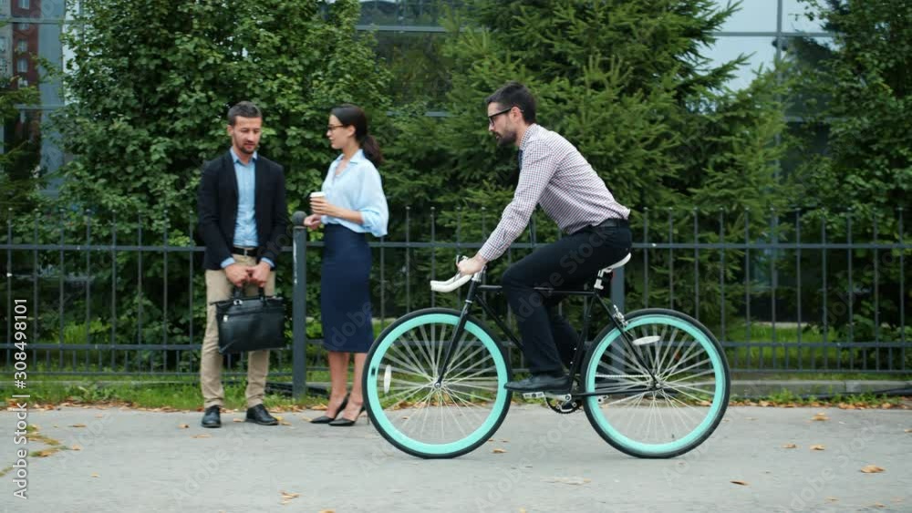 Slow motion of young male office worker riding bicycle to work near business center enjoying activity and healthy lifestyle. People, ecology and employees concept. Slow motion of young male office worker riding bicycle to work near business center enjoying activity and healthy lifestyle. People, ecology and employees concept.