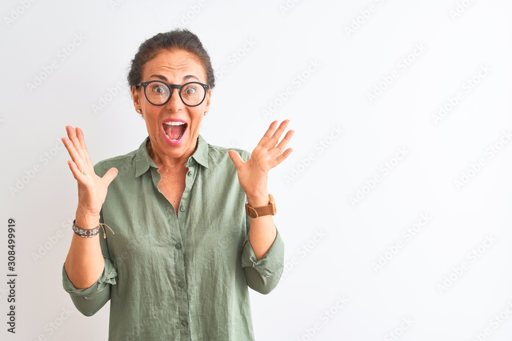 Middle age woman wearing green shirt and glasses standing over isolated white background celebrating crazy and amazed for success with arms raised and open eyes screaming excited. Winner concept Middle age woman wearing green shirt and glasses standing over isolated white background celebrating crazy and amazed for success with arms raised and open eyes screaming excited. Winner concept