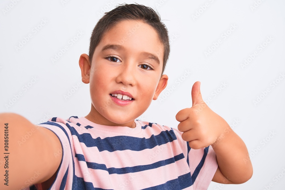 Beautiful kid boy wearing casual striped t-shirt make selfie over isolated white background happy with big smile doing ok sign, thumb up with fingers, excellent sign Beautiful kid boy wearing casual striped t-shirt make selfie over isolated white background happy with big smile doing ok sign, thumb up with fingers, excellent sign