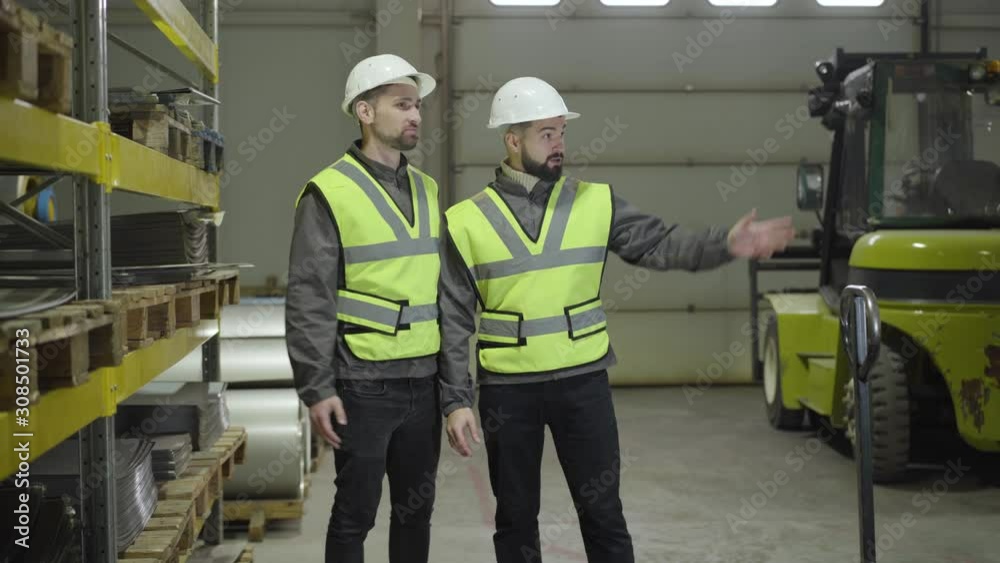 Portrait of two Caucasian male workers standing in steel plant and talking. Staff planning their working day. Employees discussing schedule and smiling. Plant, manufacture, profession, occupation. Portrait of two Caucasian male workers standing in steel plant and talking. Staff planning their working day. Employees discussing schedule and smiling. Plant, manufacture, profession, occupation.