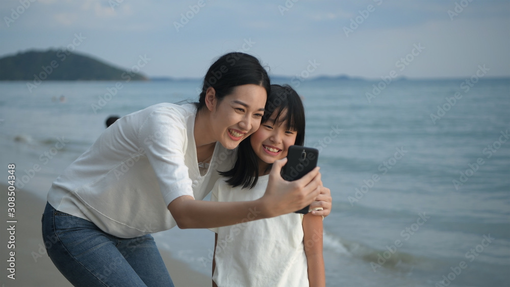 Holiday concept. Mother and daughter are taking pictures with mobile phones on the beach. 4k Resolution.