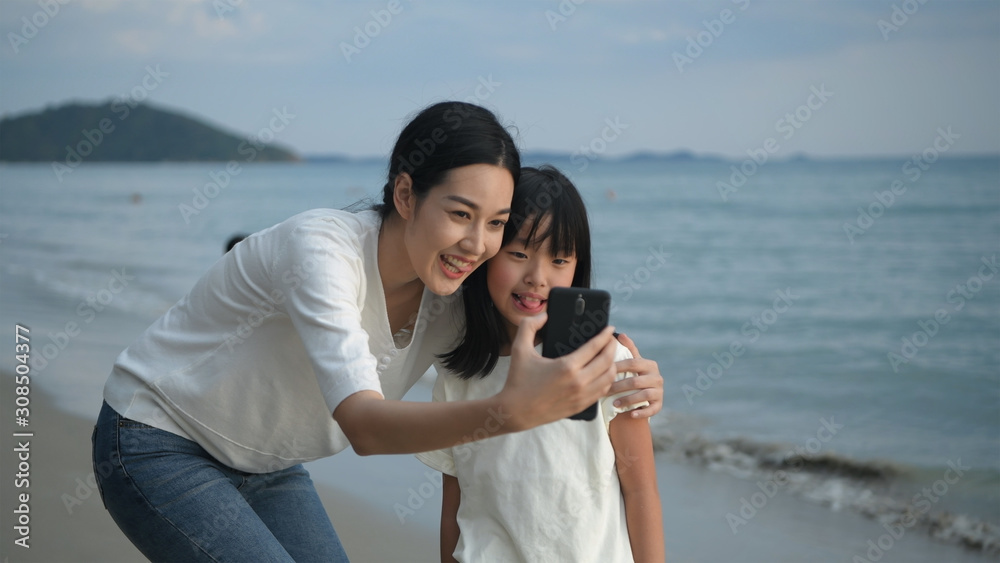 Holiday concept. Mother and daughter are taking pictures with mobile phones on the beach. 4k Resolution. Holiday concept. Mother and daughter are taking pictures with mobile phones on the beach. 4k Resolution.