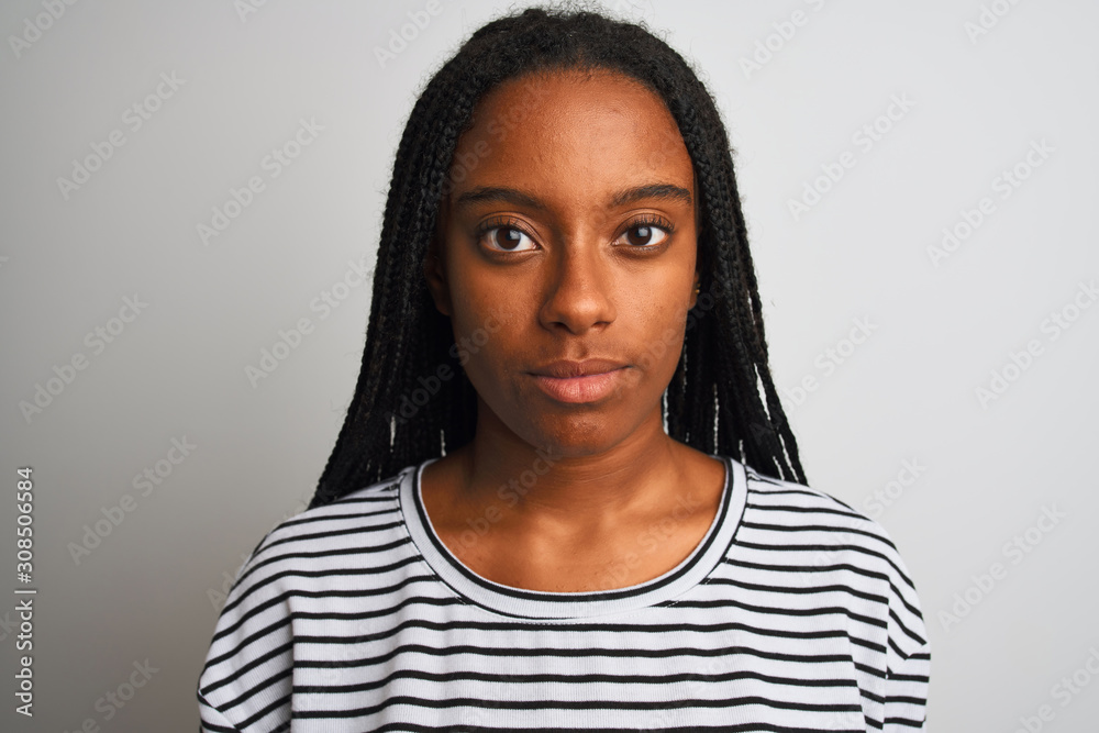 Young african american woman wearing striped t-shirt standing over isolated white background with a confident expression on smart face thinking serious Young african american woman wearing striped t-shirt standing over isolated white background with a confident expression on smart face thinking serious