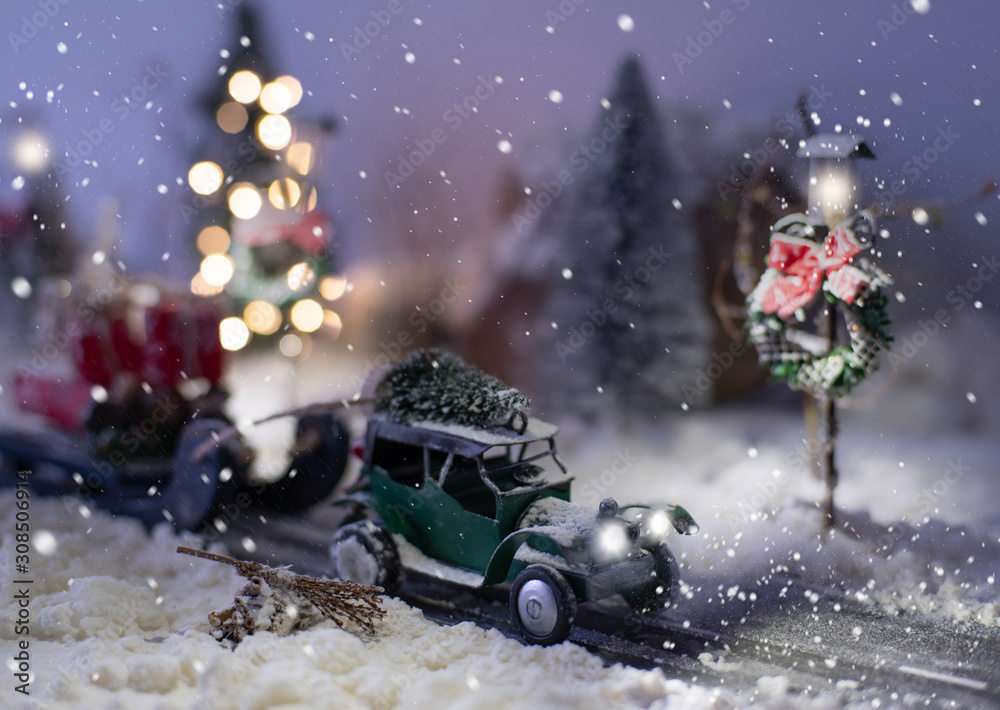 Miniature classic car carrying a christmas tree and gifts on snowy road in winter background Miniature classic car carrying a christmas tree and gifts on snowy road in winter background
