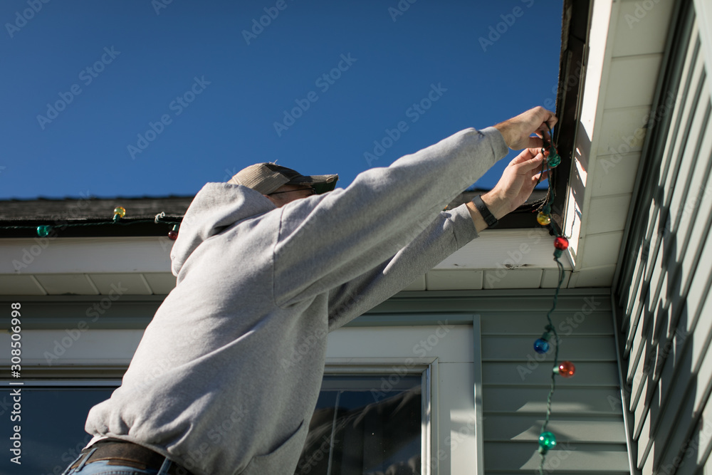 Man hanging exterior christmas lights on gutters