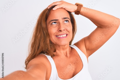 Middle age mature woman taking a selfie photo using smartphone over isolated background stressed with hand on head, shocked with shame and surprise face, angry and frustrated. Fear and upset 