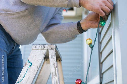 Close up of man on ladder hanging Christmas lights on house
