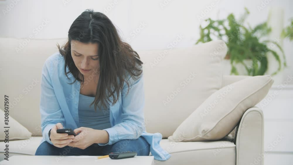 Admirable woman is concentrated on using her smartphone, while sitting on the sofa, at home. Slow motion. Copy space. 4K. Admirable woman is concentrated on using her smartphone, while sitting on the sofa, at home. Slow motion. Copy space. 4K.