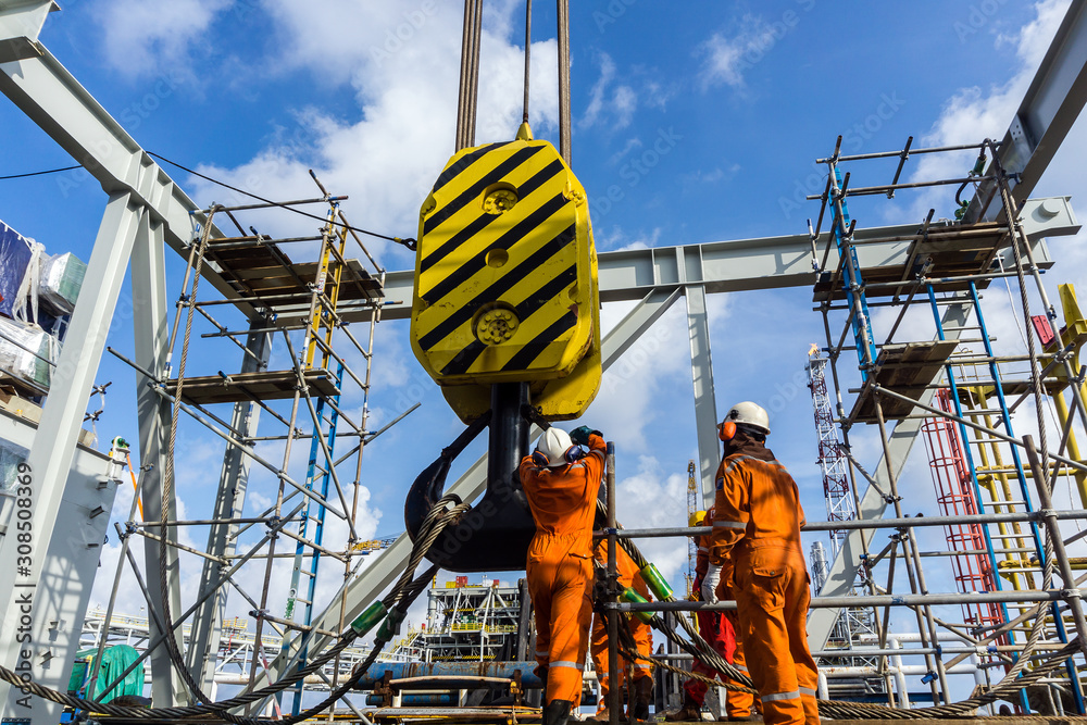 Offshore workers performing inspection to a crane hook and rigging arrangement prior to heavy lift