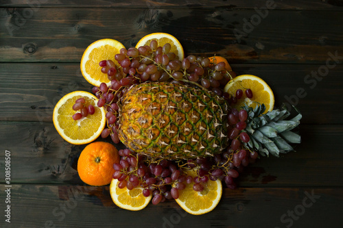 pineapple  oranges and pink grapes lie on a wooden table