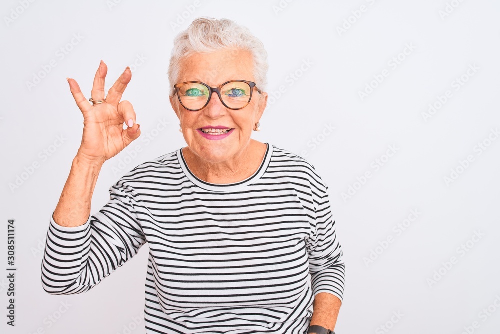Senior grey-haired woman wearing striped navy t-shirt glasses over isolated white background smiling positive doing ok sign with hand and fingers. Successful expression. Senior grey-haired woman wearing striped navy t-shirt glasses over isolated white background smiling positive doing ok sign with hand and fingers. Successful expression.