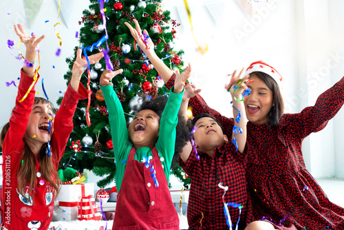 Asian mother or teacher and her children spend a great time on a holiday near the Christmas tree, having fun with confetti., Christmas time