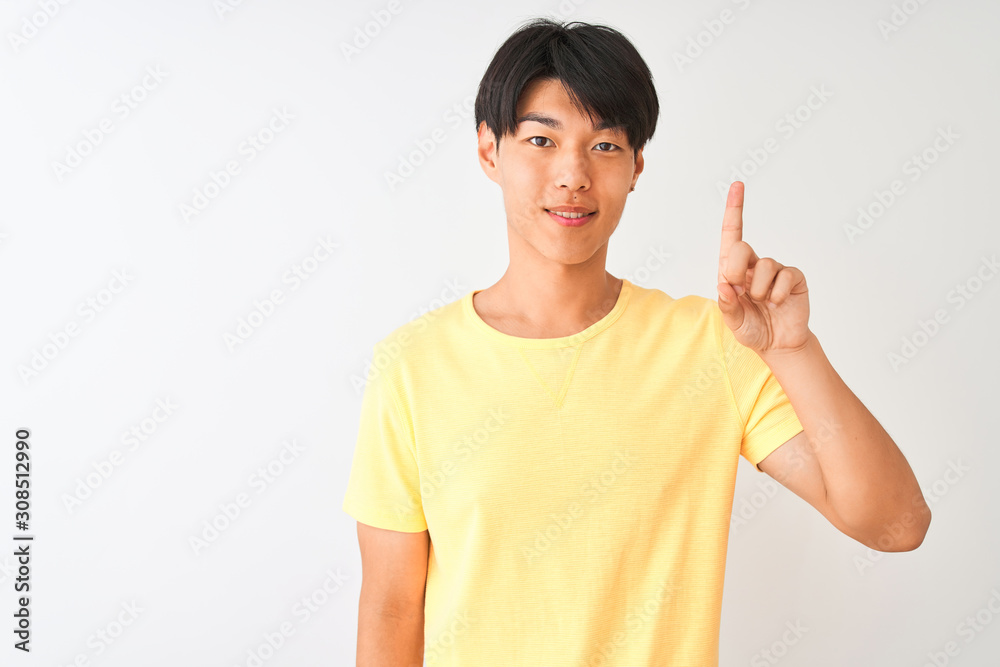 Chinese man wearing yellow casual t-shirt standing over isolated white background showing and pointing up with finger number one while smiling confident and happy. Chinese man wearing yellow casual t-shirt standing over isolated white background showing and pointing up with finger number one while smiling confident and happy.