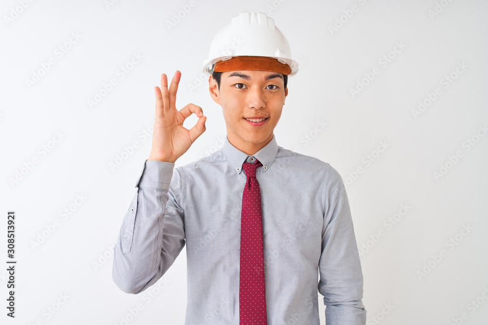 Chinese architect man wearing tie and helmet standing over isolated white background smiling positive doing ok sign with hand and fingers. Successful expression. Chinese architect man wearing tie and helmet standing over isolated white background smiling positive doing ok sign with hand and fingers. Successful expression.