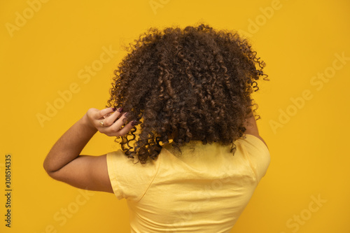 Obraz na plátne Backwards American African woman with her curly hair on yellow background