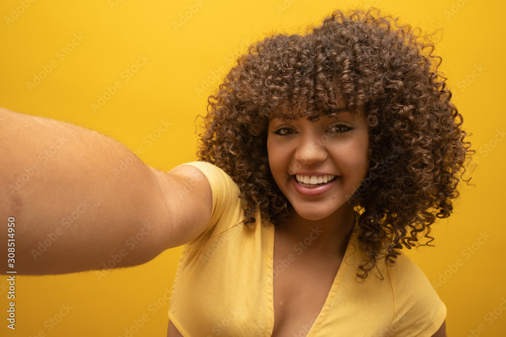 Close up of excited young african american girl in fur sweater posing isolated on yellow orange background in studio. People lifestyle concept. Mock up copy space. Doing selfie shot on mobile phone. Close up of excited young african american girl in fur sweater posing isolated on yellow orange background in studio. People lifestyle concept. Mock up copy space. Doing selfie shot on mobile phone.