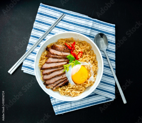Instant Noodle with fried pork pepper and egg in the bowl on black background. Top view.